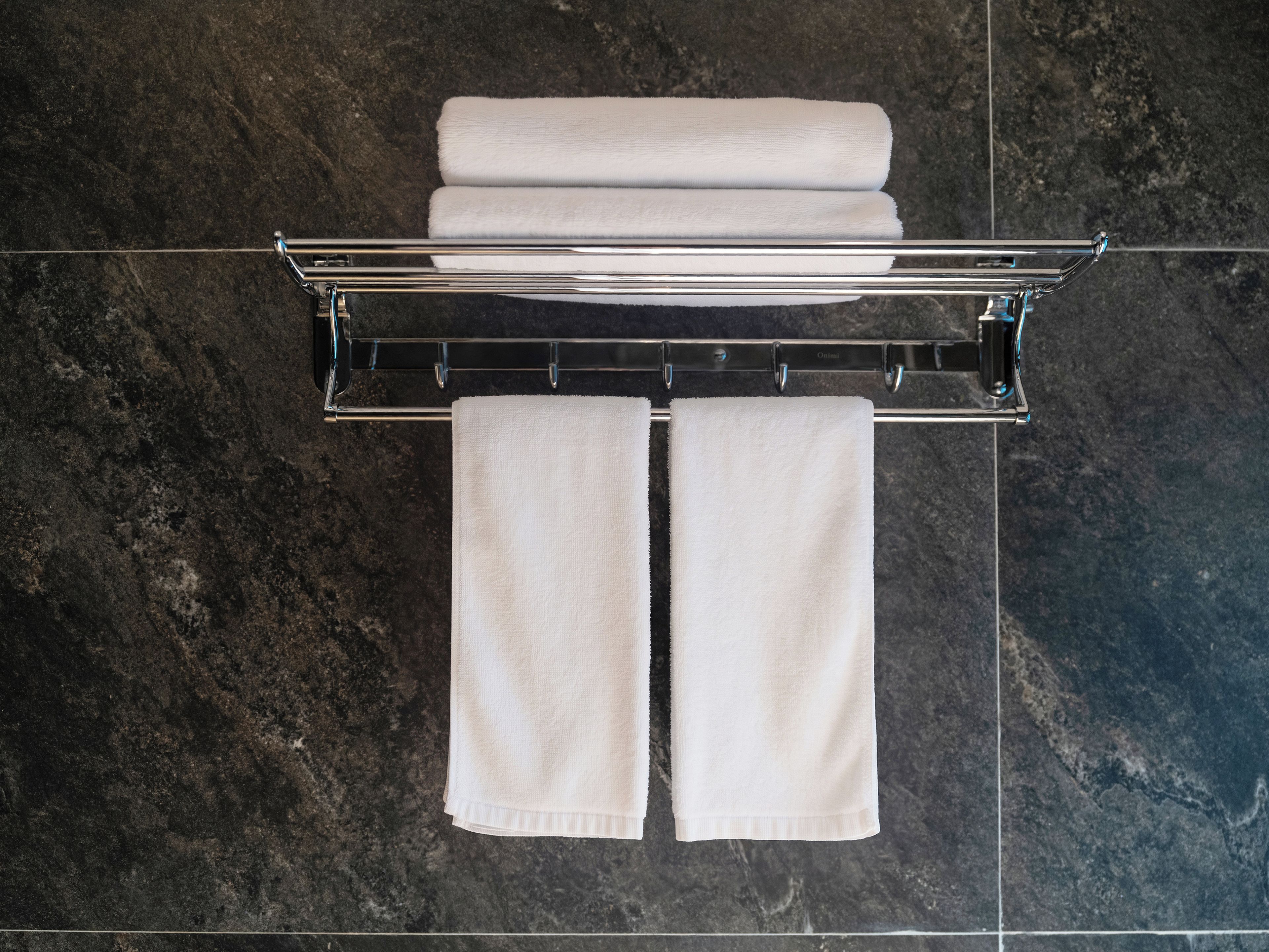 A bathroom with a towel rack holding three folded towels and two towels hanging below.