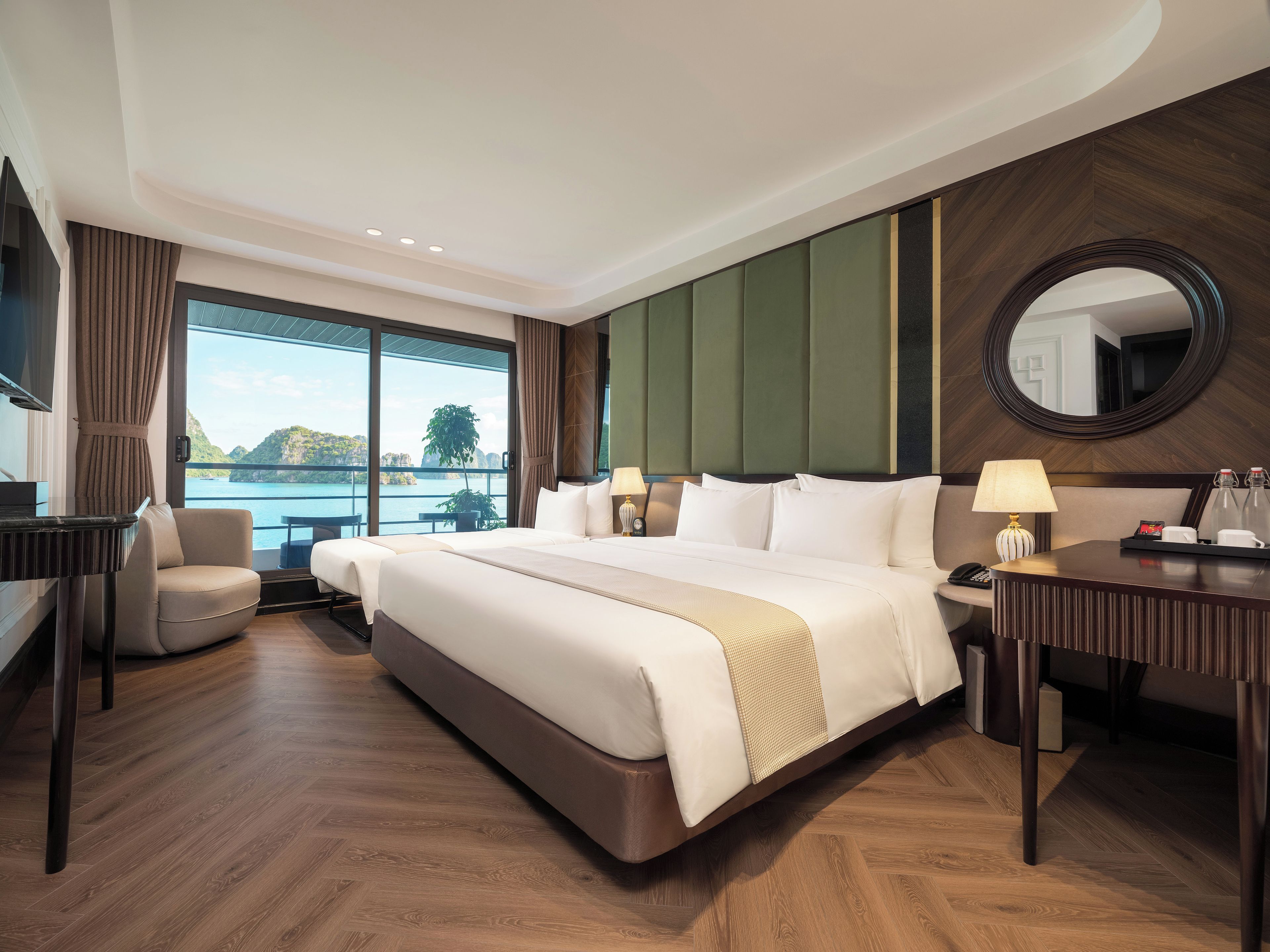 A hotel room with a large bed, a desk, a chair, a mirror, and a view of a body of water.