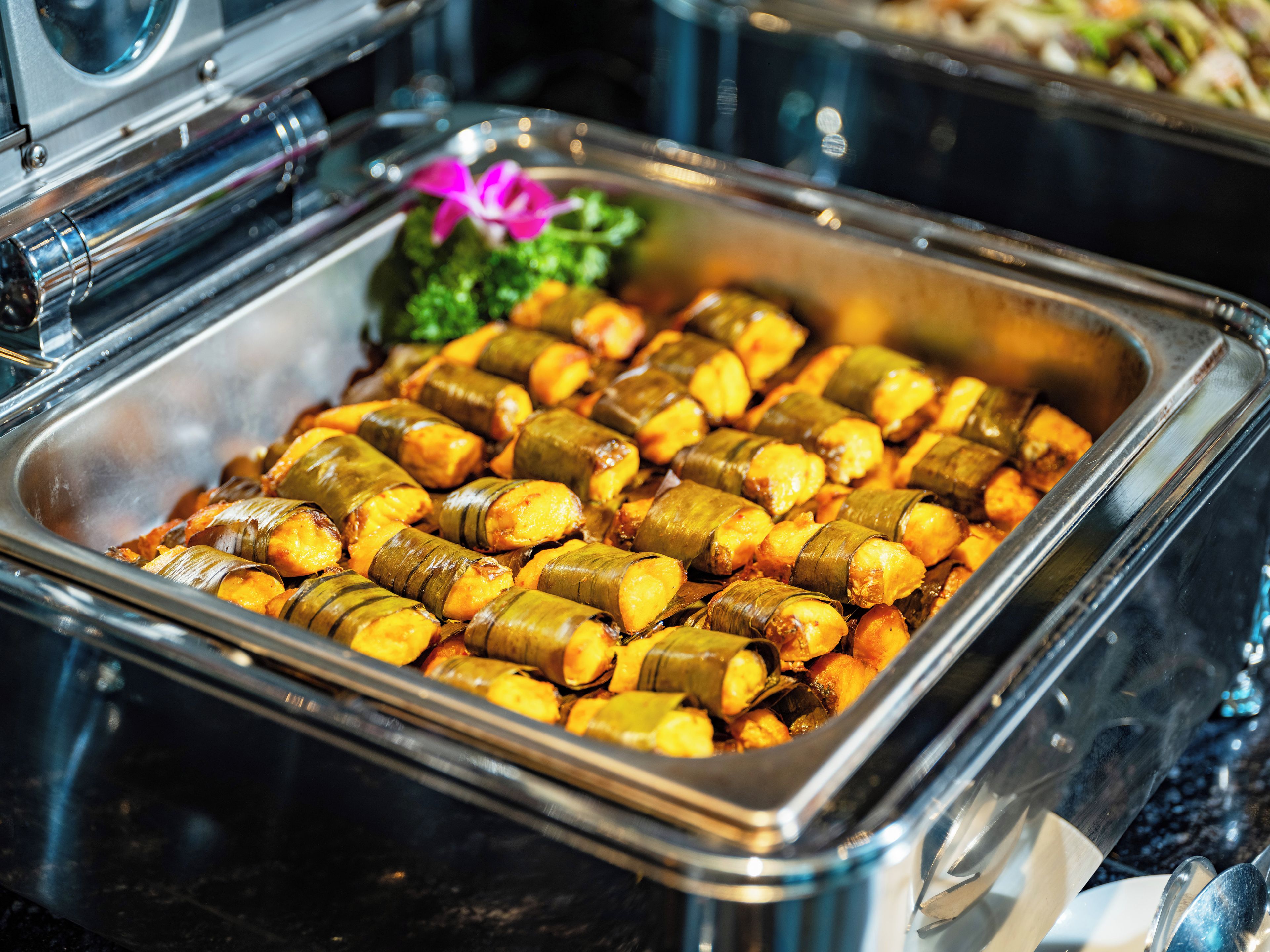 Un bufé con una variedad de platos, incluyendo una sección con comida envuelta en hojas.