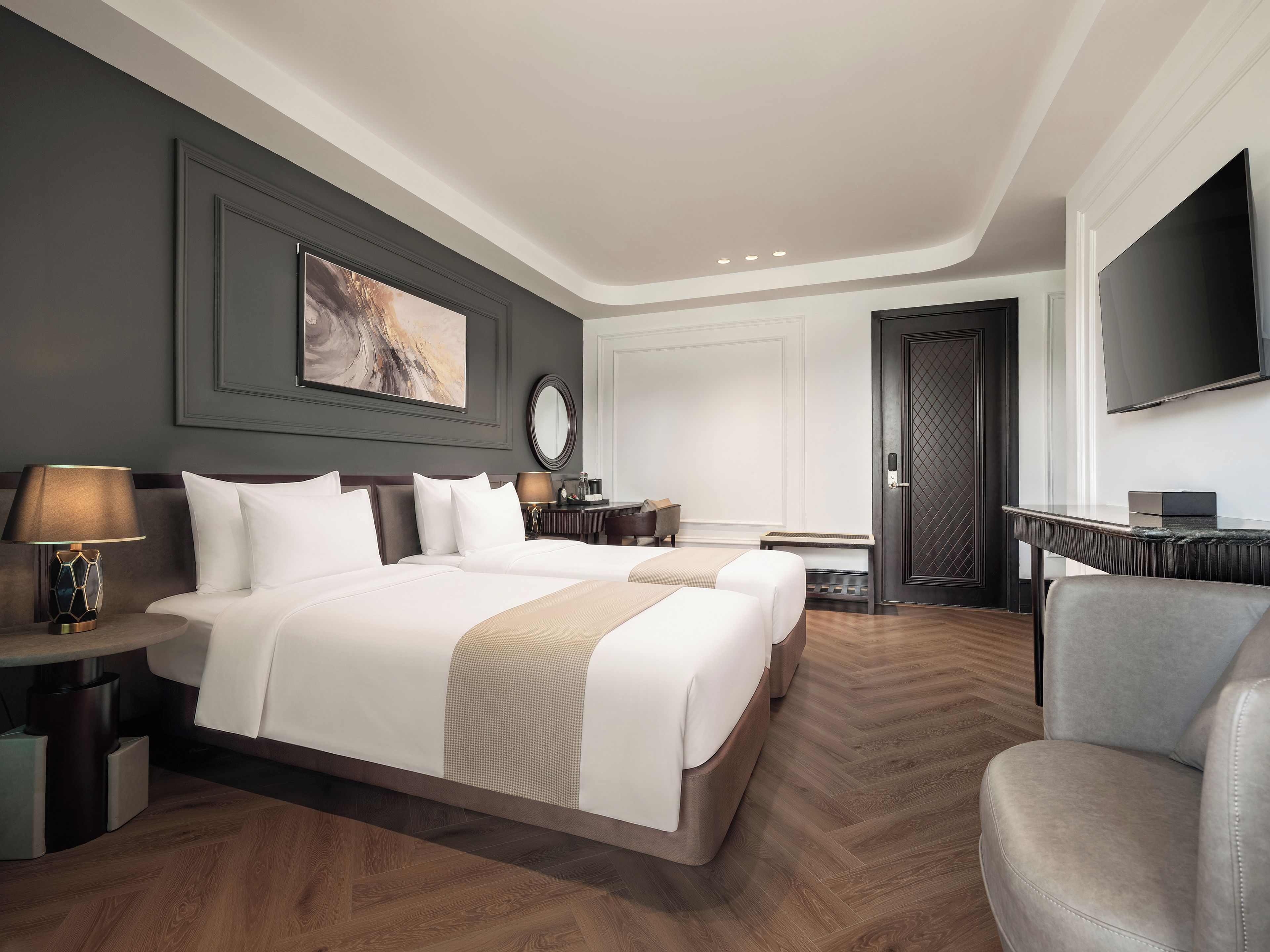 A hotel room with two beds, a desk, a chair, a TV, and a large painting on the wall.