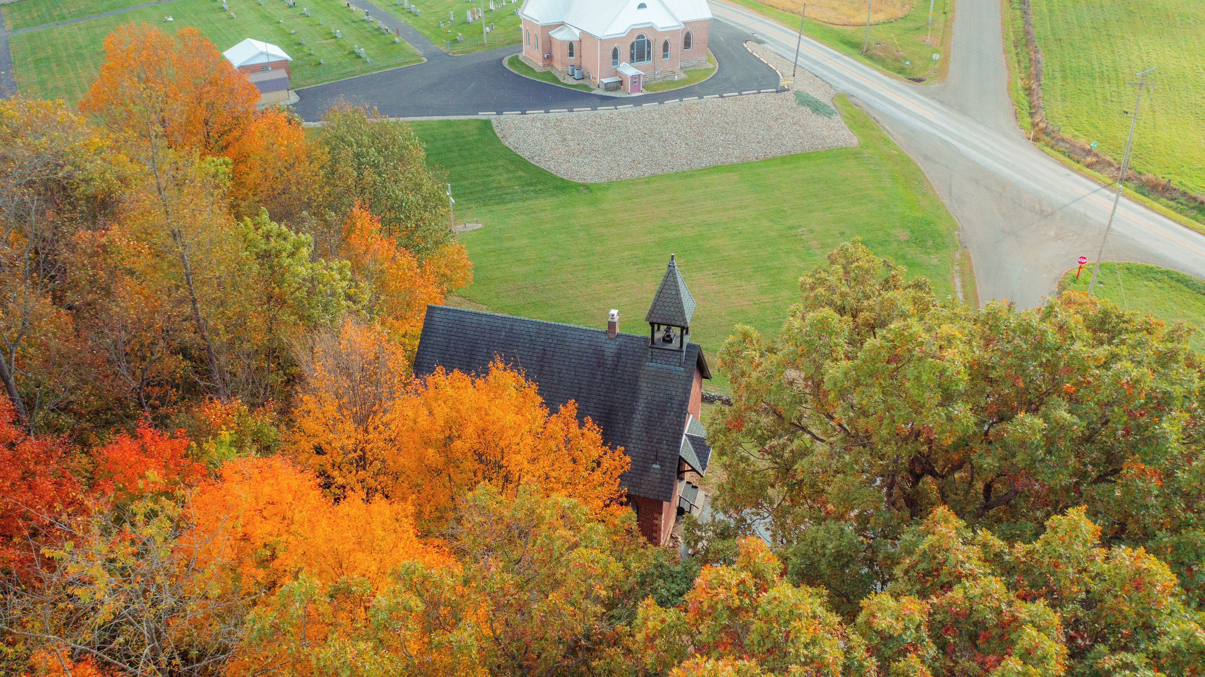 An aerial view of a church with a bell tower, surrounded by autumn foliage.