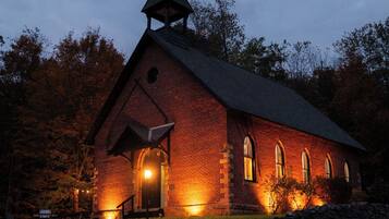 Une église en briques, dotée d’un clocher, de fenêtres illuminées et d’un chemin de gravier devant l’entrée.