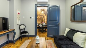 Una sala de estar con televisor, una mesa de centro de madera, un sofá negro y un área de comedor visible a través de un umbral abierto.