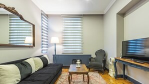 Una sala de estar con un sofá negro, una mesa de centro de madera, un televisor y una lámpara.