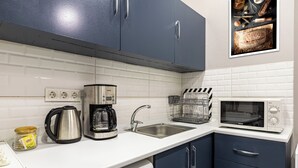 Una cocina con encimeras blancas, cafetera, hervidor, microondas y fregadero.