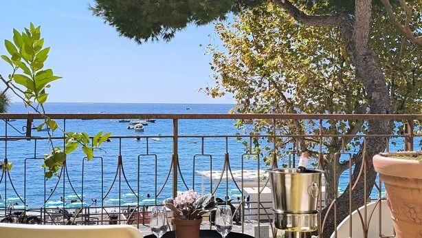 Una terraza con vista al mar, que incluye una mesa con una planta en maceta y un recipiente metálico.