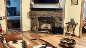 Una sala de estar acogedora con chimenea de piedra, sofá de cuero y televisor montado en la pared.