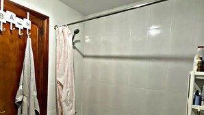 Une salle de bain équipée d’une baignoire, d’un rideau de douche, d’un porte-serviettes avec des serviettes et d’une étagère contenant des articles de toilette.