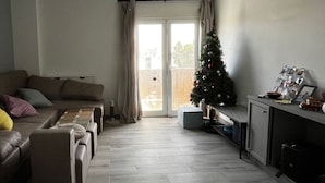 Un salon avec un canapé, une table basse, un petit sapin de Noël et un meuble contenant divers objets.