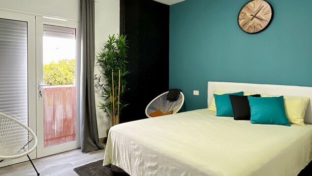 Une chambre à coucher avec un lit, une horloge au mur, une chaise et une plante.
