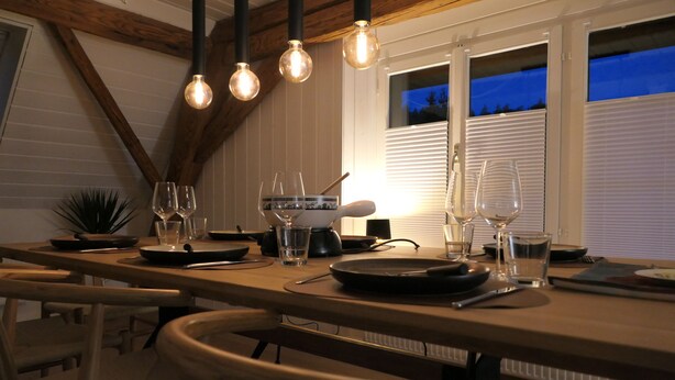 Een eetruimte met een houten tafel, stoelen en hangende lampen.