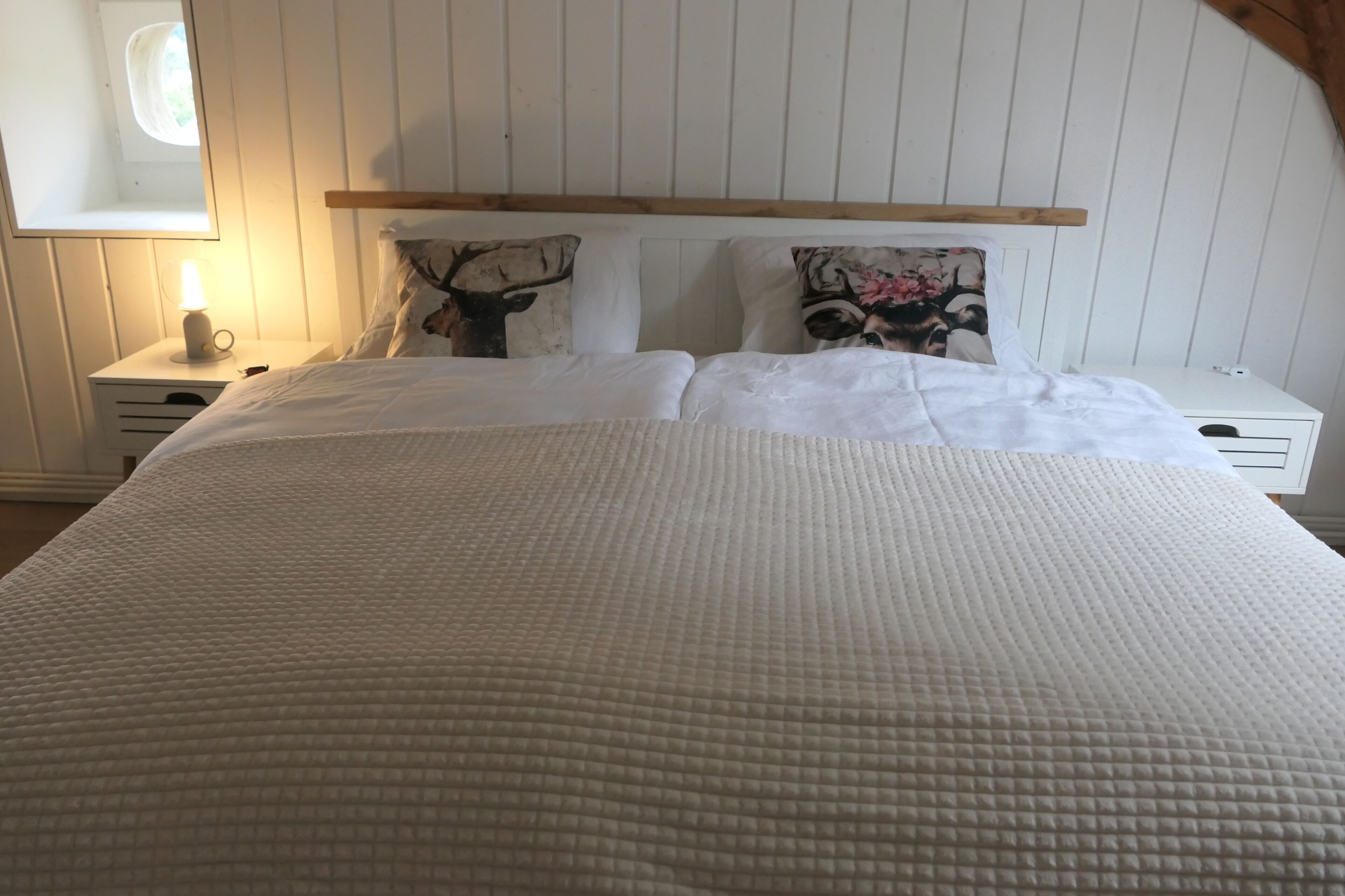 Un letto con copriletto trapuntato, due cuscini fantasia animalier, un comodino con una lampada e una testiera in legno.