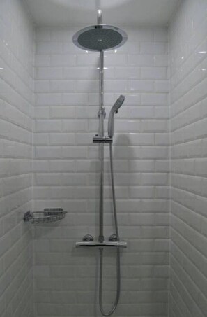 Une douche équipée d’un pommeau de douche à main et d’un robinet mural, dans une pièce carrelée.
