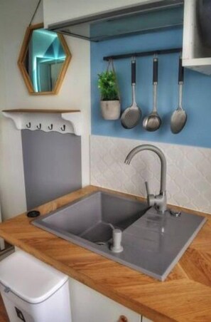 Une cuisine dotée d’un évier moderne, d’un plan de travail en bois et d’un crédence ornée de casseroles suspendues.