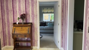 Un pasillo con un aparador de madera, un florero con flores y vista a una sala de estar con sofá y papel tapiz estampado.