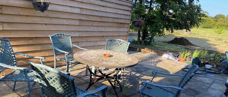 A patio with a round table and four chairs, a hanging flower pot, and a wooden wall in the background.