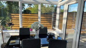 Un invernadero con puerta de cristal, una mesa con sillas y un jarrón con flores.