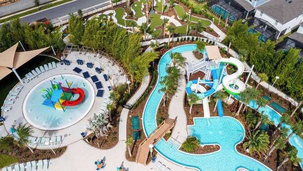An aerial view of a resort with a large swimming pool, a water slide, and a lazy river.