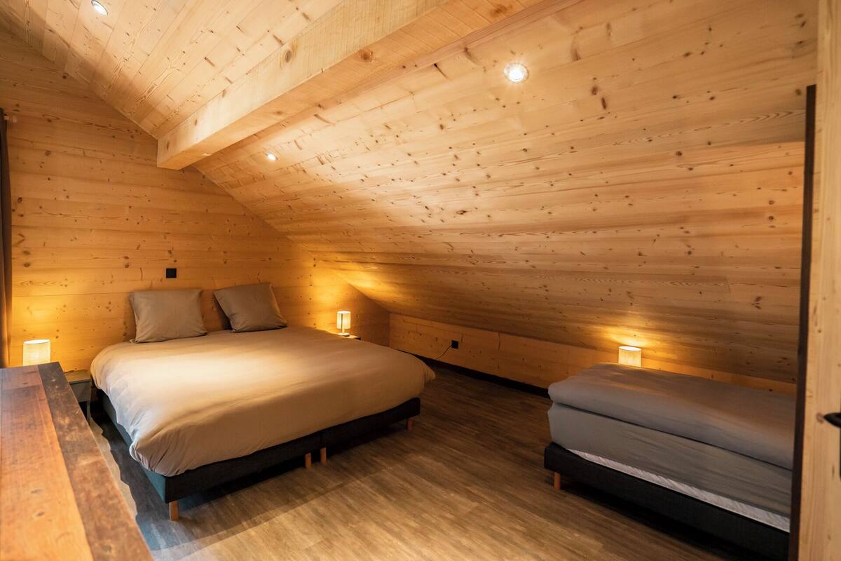 Ein gemütliches Schlafzimmer im Dachgeschoss mit Holzbalkendecke, einem großen Bett, zwei Nachttischen und einer Bank.