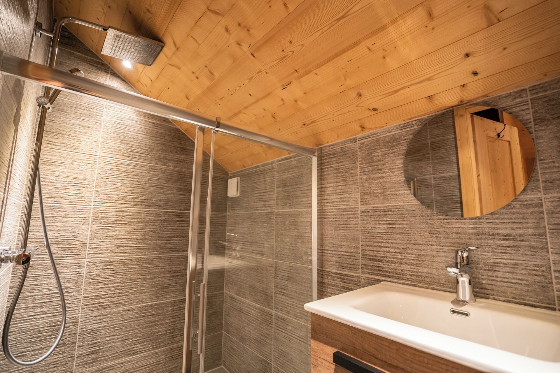 Un bany modern amb dutxa, un lavabo i un sostre de fusta.