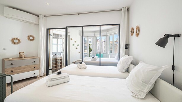 A modern hotel room with two beds, a desk, and a view of the city through large windows. - Cozy 2 Bedroom Apartment in the Heart of Cannes (Cannes)