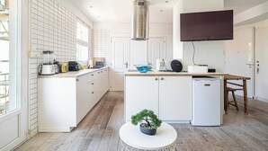 A modern kitchen with white cabinetry, a central island, a built-in stove, and a flat-screen TV mounted above the island. - Cozy 2 Bedroom Apartment in the Heart of Cannes (Cannes)