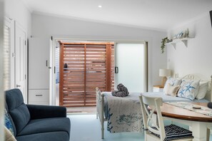 A room with a bed, a dining table, a sofa, and a sliding door leading to an outdoor area. - Blue Cottage Ulladulla | 3 Min Walk to Beach | Sleeps 12 | Pet Friendly (Ulladulla)
