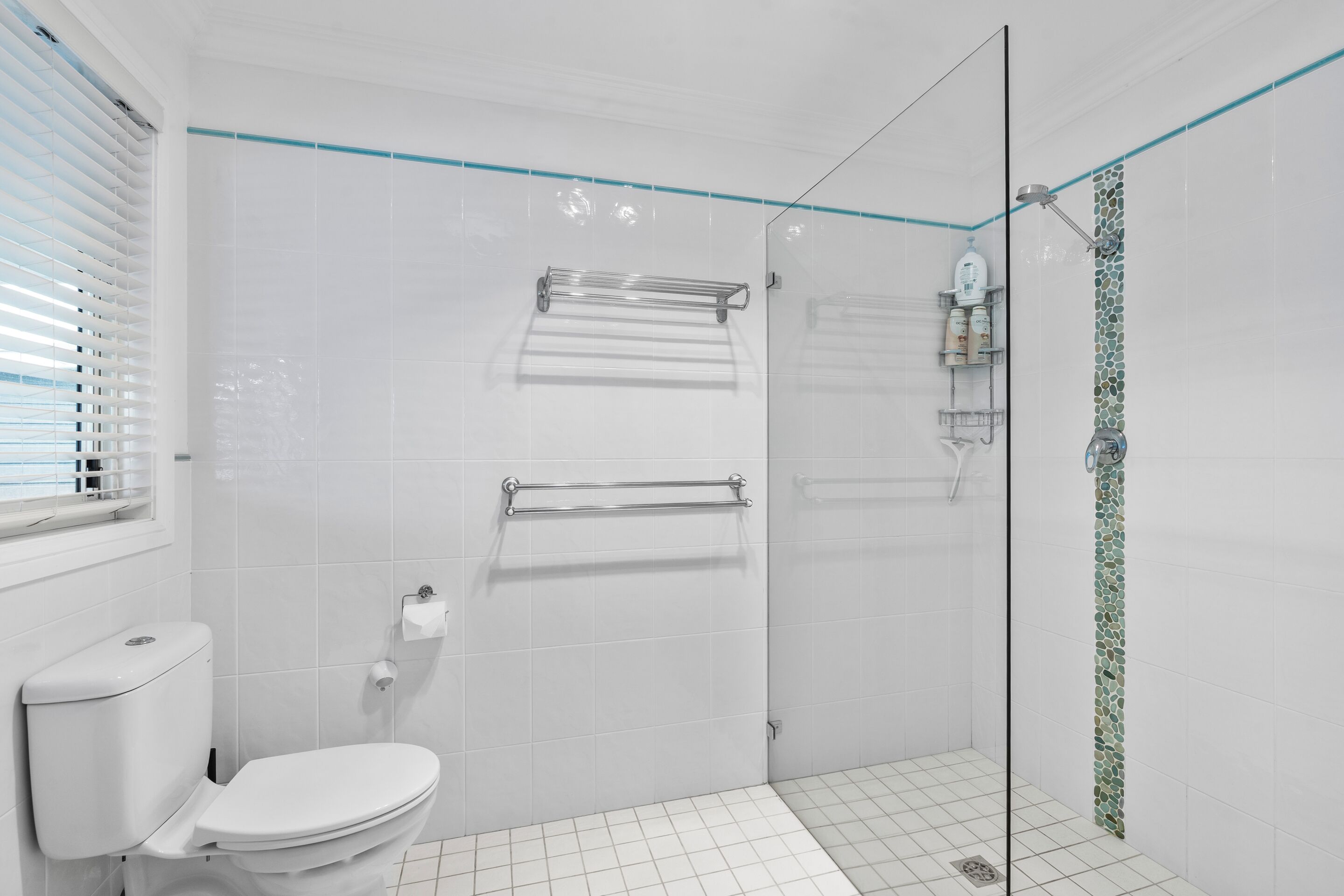A modern bathroom with a glass shower enclosure, white tiled walls, and a toilet.