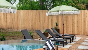 Zona de piscina con sillones de descanso, una terraza de madera y una planta de cactus.