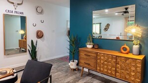Un salón moderno con una pared de acento color turquesa, un mueble de madera con diseños geométricos, un espejo y una silla negra.