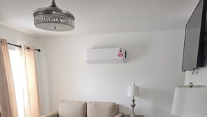 Ein modernes Wohnzimmer mit einem beigen Sofa, einem schwarzen Bürostuhl, einem kleinen Beistelltisch mit einer Lampe und einem Deckenventilator.
