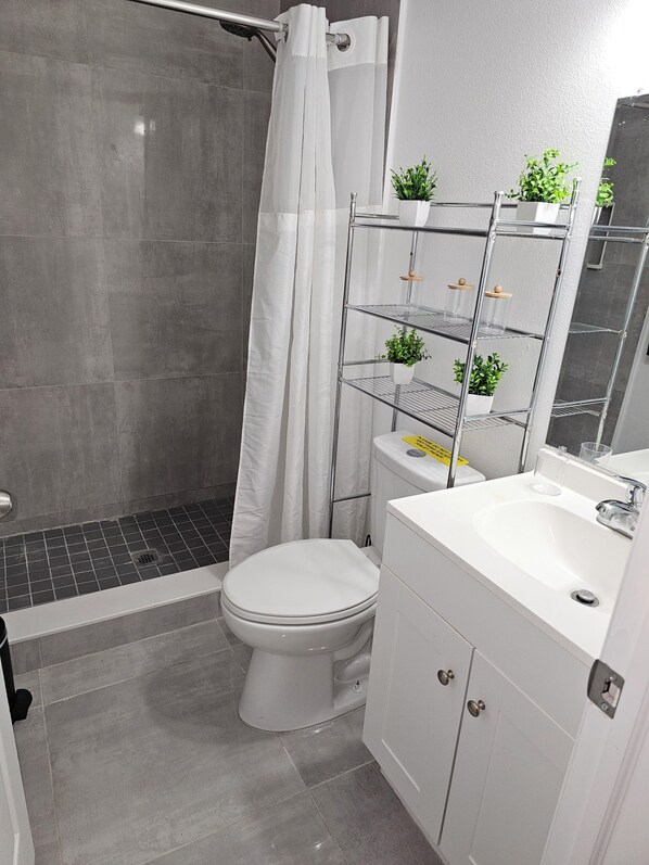 A bathroom with a shower, toilet, and a white sink with a mirror above it. There are potted plants on a metal shelf above the sink. - Quiet and safe neighborhood come to this great place with lots of room for relax (Orlando)