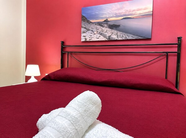 Una cama con cabecera roja, almohada y toalla blancos.