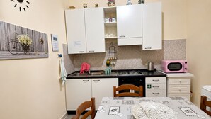 Une cuisine de taille réduite avec des meubles blancs, un micro-ondes rose et une table à manger recouverte d’une nappe à motifs.