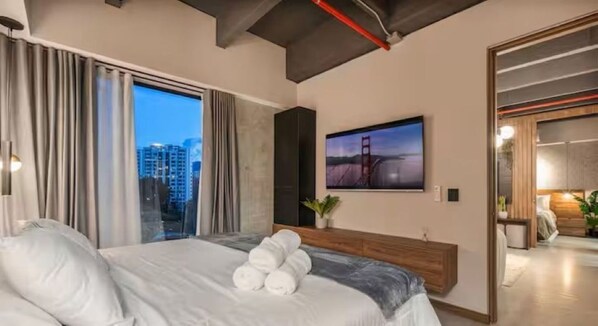 A modern hotel room with a large bed, a flat-screen TV, a city view, and a wooden headboard. - Mixa Open Community (Medellín)