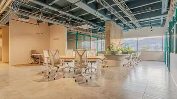 A spacious office with a high ceiling, exposed ductwork, and large windows offering a view of the city.