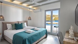 Un dormitorio moderno con una cama grande, dos lámparas colgantes, vista al mar y una mesita con un objeto decorativo.