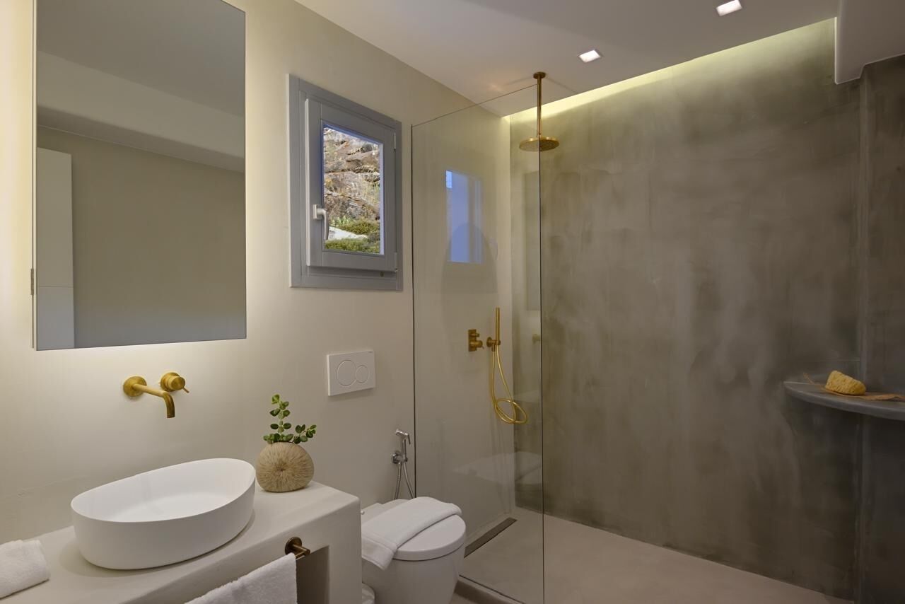 A modern bathroom with a large oval sink, a toilet, and a glass-enclosed shower with gold fixtures.