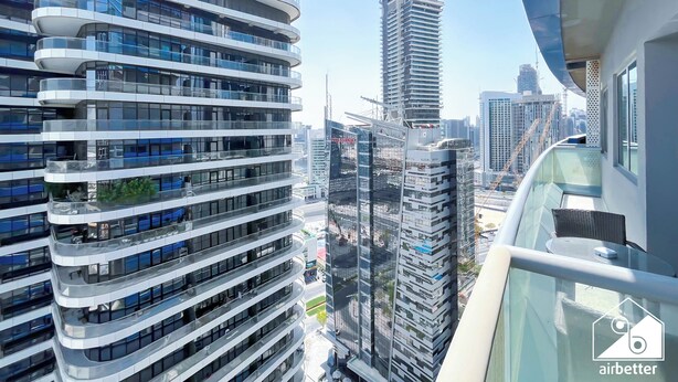 A modern high-rise building with multiple balconies, large windows, and a construction crane in the background. - Elegant 2-bed Retreat Stunning Downtown Views (Dubai)