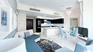 A modern living room with a sofa, a glass coffee table, and a dining area with a TV and a computer. - Elegant 2-bed Retreat Stunning Downtown Views (Dubai)