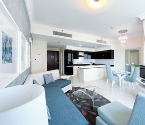 A modern living room with a sofa, a glass coffee table, and a dining area with a TV and a computer. - Elegant 2-bed Retreat Stunning Downtown Views (Dubai)