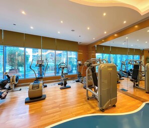 A gym with various exercise machines, large windows, and a mirror reflecting the equipment. - Elegant 2-bed Retreat Stunning Downtown Views (Dubai)