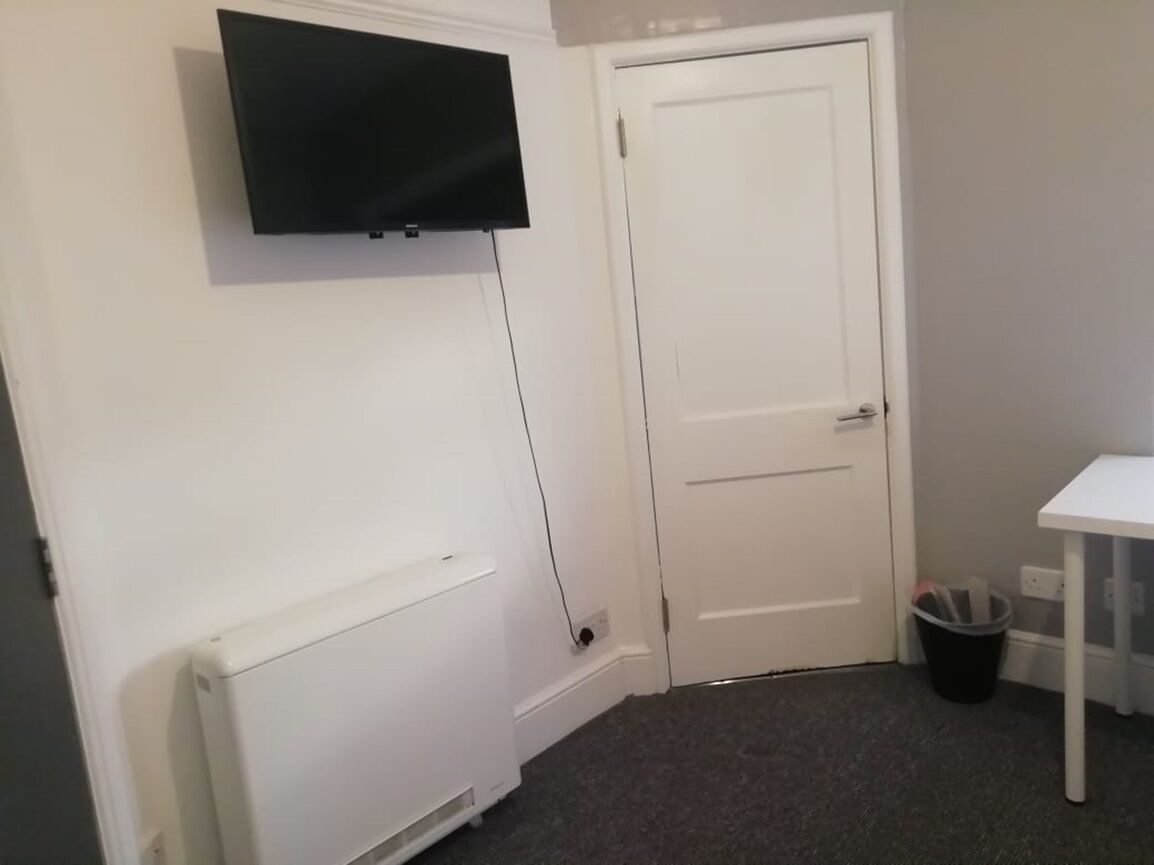 Une pièce avec un radiateur blanc, une porte blanche, une table blanche et une poubelle noire.