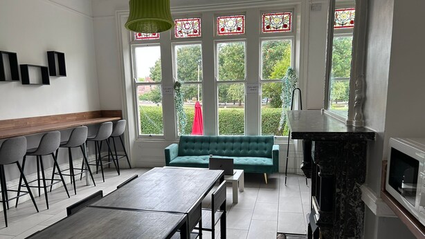 A modern kitchen with a dining area, a teal sofa, and a bar with stools. - Green Lodge (Liverpool)