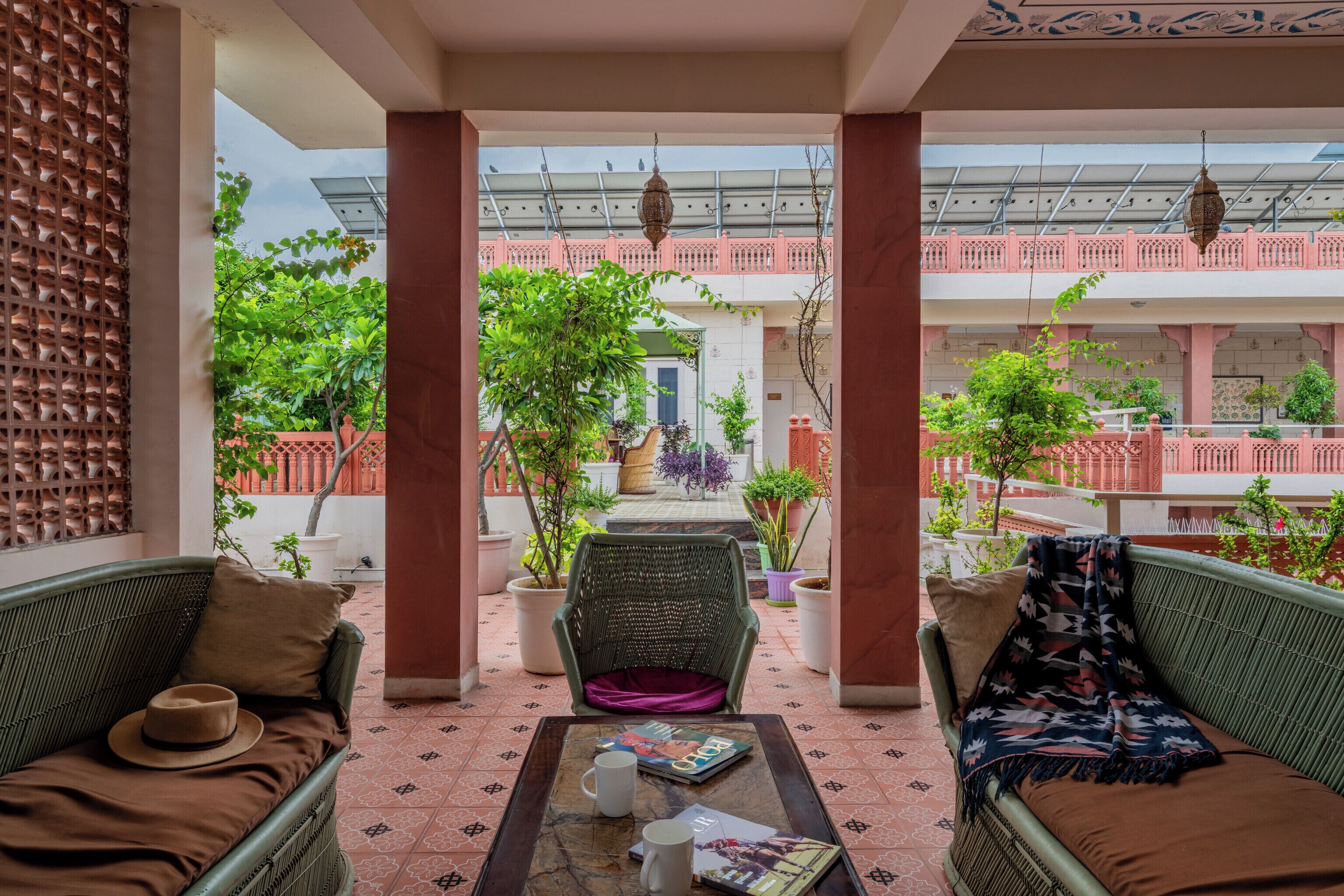 A covered outdoor seating area with wicker furniture, a table with a magazine and a mug, and potted plants.
