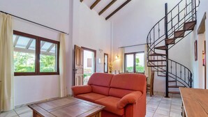 A living room with a sofa, a wooden table, a spiral staircase, and large windows. - Ibipozo Bungalow in Pozo Alcon (Pozo Alcon)