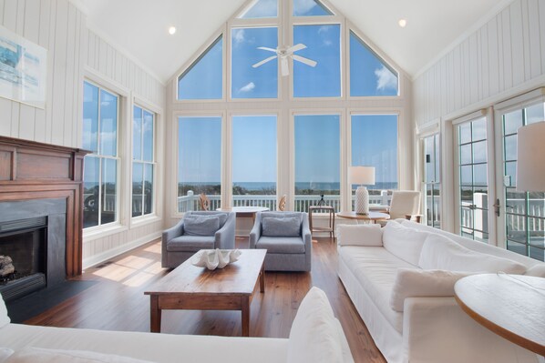 A spacious living room with a fireplace, large windows, and a view of the ocean.