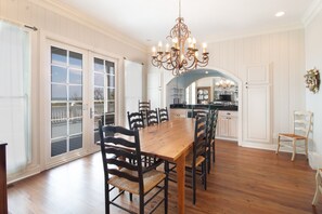 A spacious dining area with a wooden table and chairs, a chandelier, and a view through large windows.