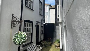 Un callejón estrecho con edificios blancos, un banco y una planta colgante.