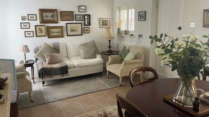 Una sala de estar con sofá, sillones, una mesa de comedor y un jarrón con flores.